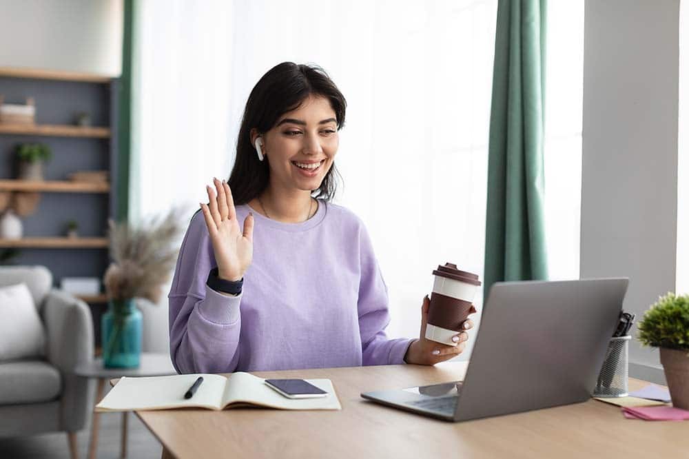 Online Meeting. Happy young woman using laptop computer for virtual conferencing, having video call at home. Cheerful millennial female in earphones communicating with colleagues or friends remotely