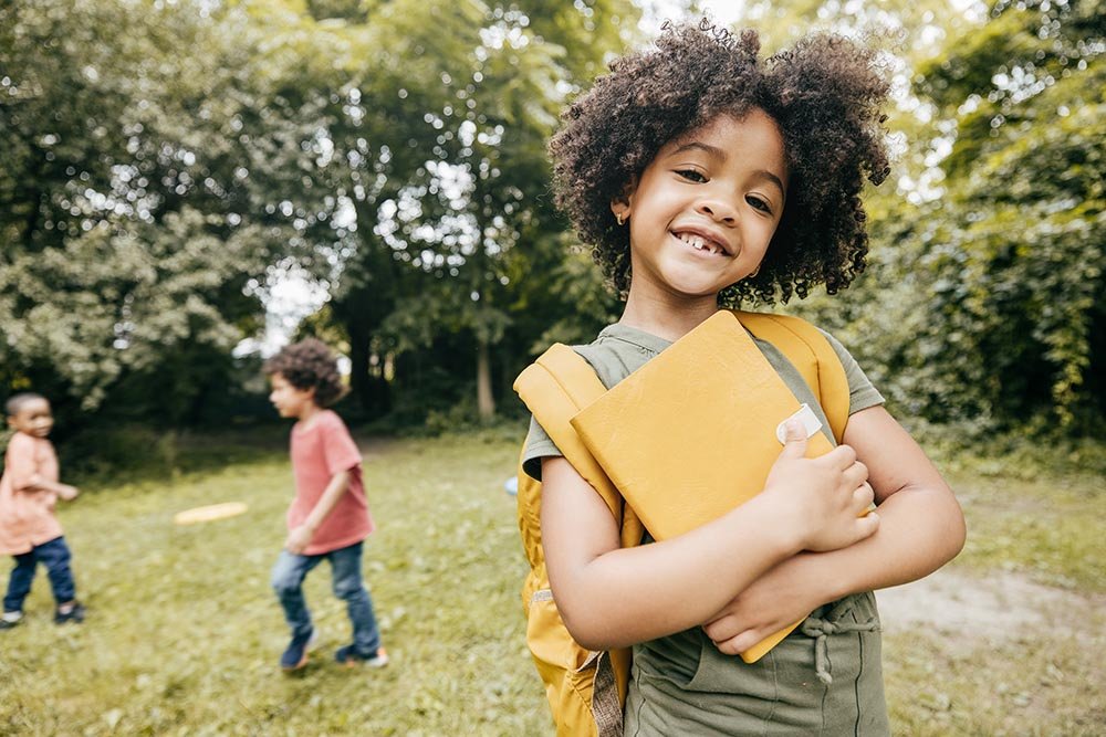 Shot of cute elementary school girl smiling and looking at camera meanwhile her school friends are in the background.